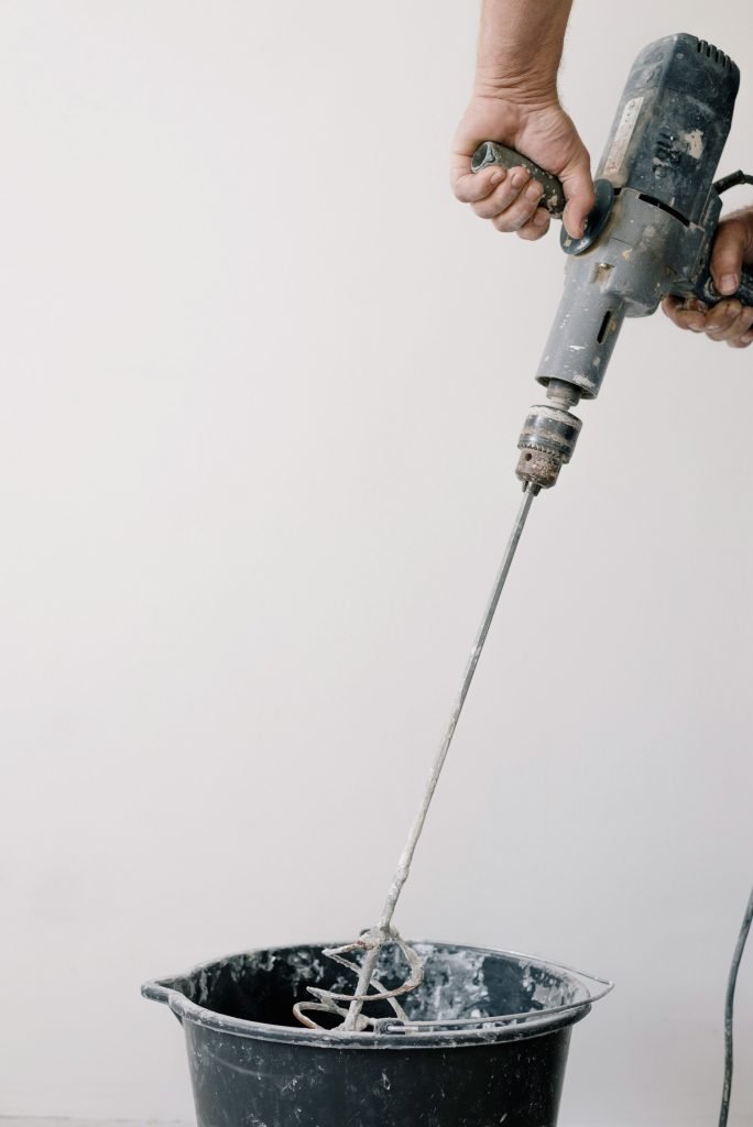 man mixing cement in a bucket with a drill